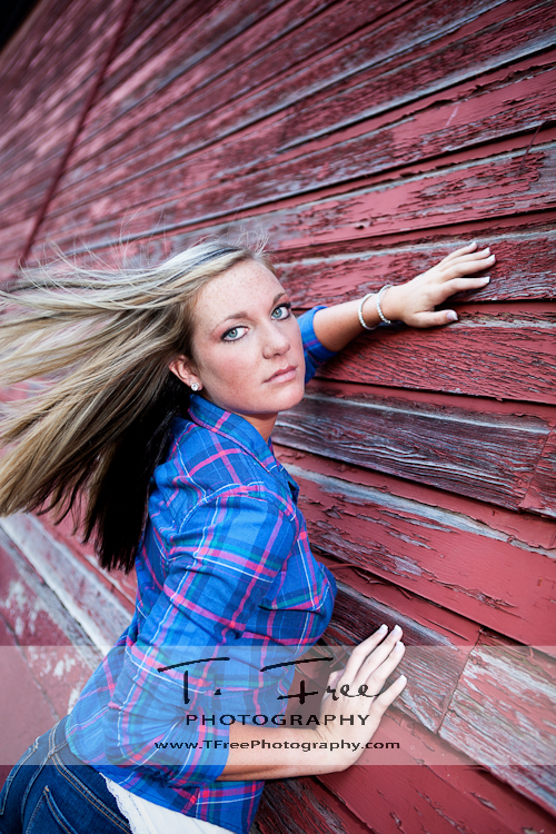 Wind blown hair senior photo standing next to an old red barn near Omaha Nebraska.