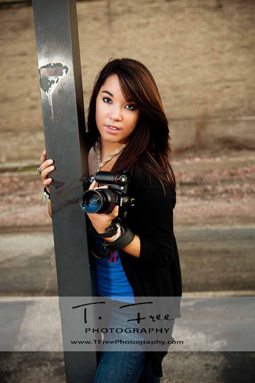 Outside senior picture of aspiring photographer with her camera as a prop taken near downtown train station in Omaha Nebraska. 